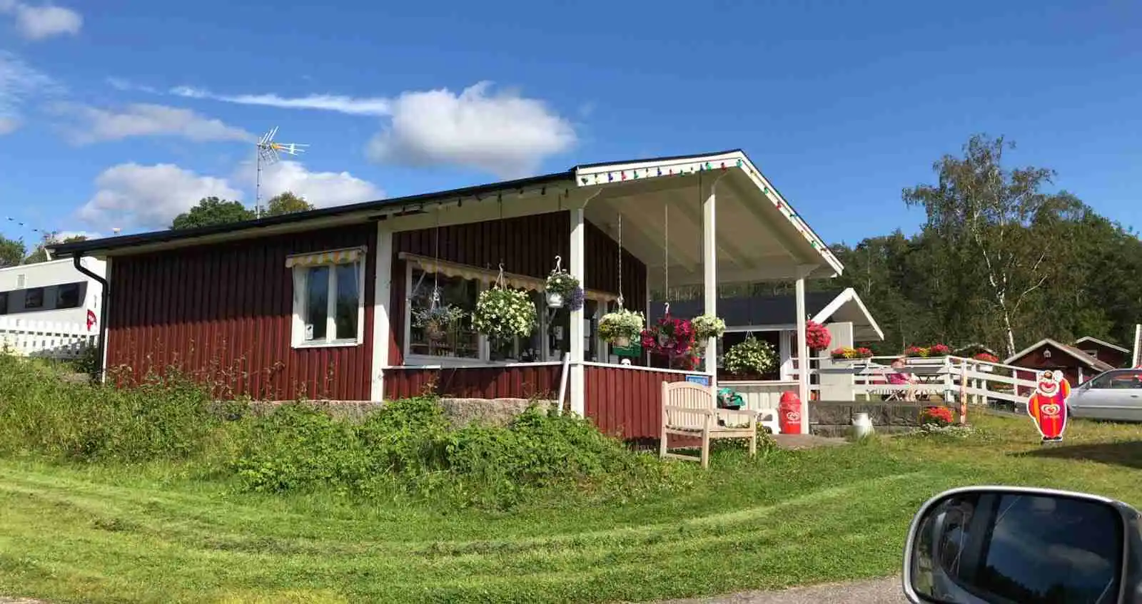 En mysig stuga på Tanums Camping och Stugby omgiven av en lummig gård med grönt gräs. Stugan har en veranda med skugga som skyddar mot solen.