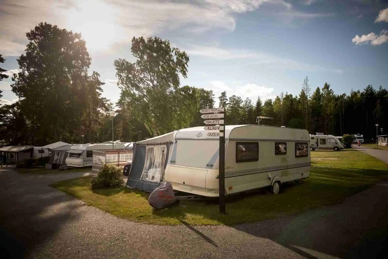 En campingplats med husvagnar och husbilar uppställda i en parkmiljö, omgiven av grönska på Bredsands Bad & Camping.
