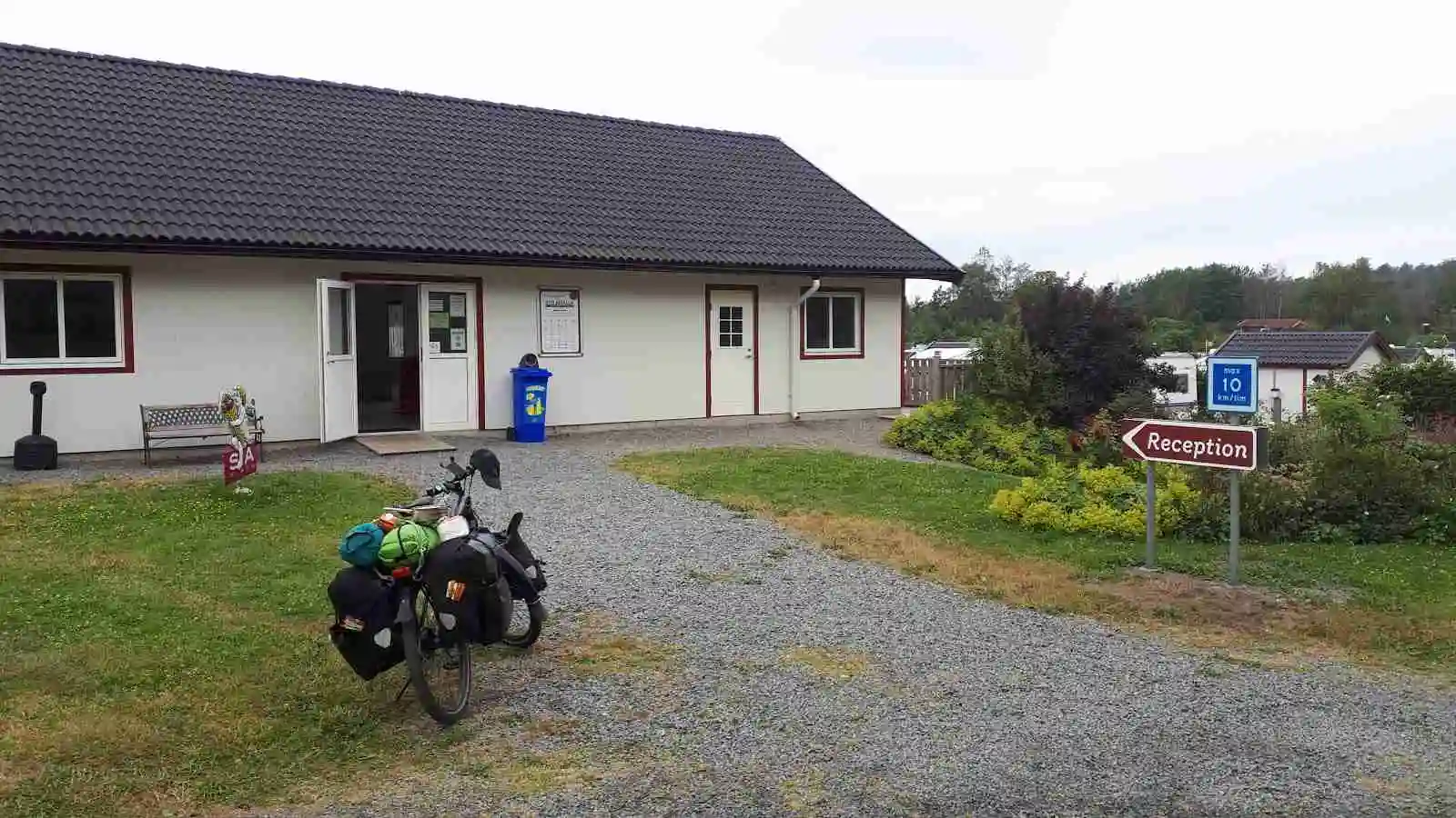 Ett lantligt stugområde vid Stråvalla Camping med små hus med sadeltak, omgivna av grönska. En mindre uppfart och en carport finns i förgrunden.