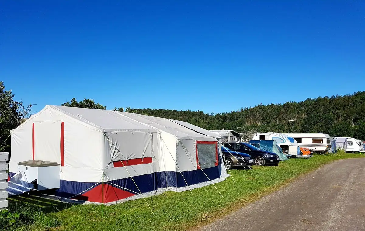 Bild av Ylserød Camping med flera tält uppställda, där ett större skyddstak av presenning är rest som sol- eller regnskydd.