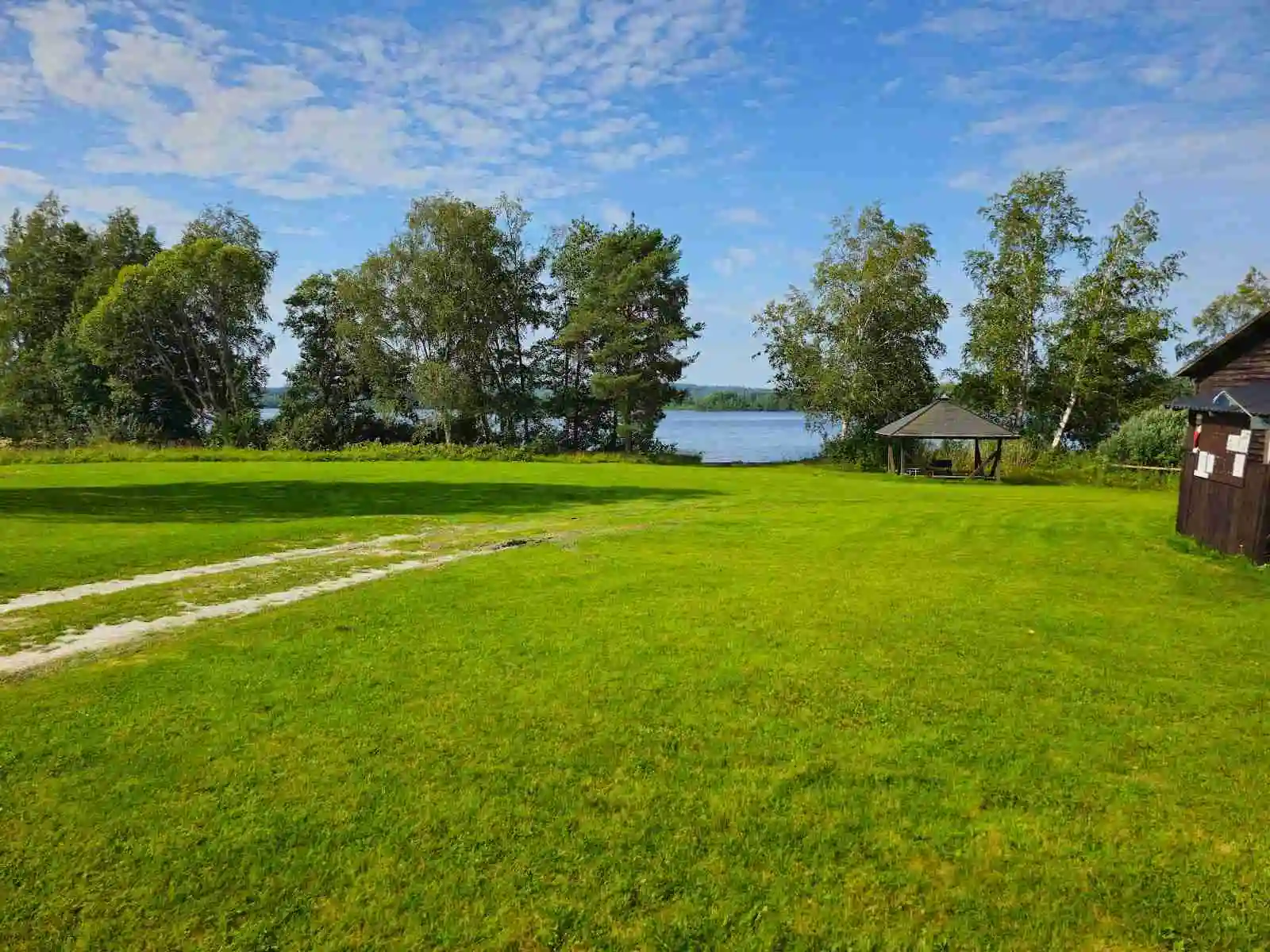 En grön och vidsträckt äng under en lätt molnig himmel, omgiven av naturlandskap vid Vreten Kursgård.