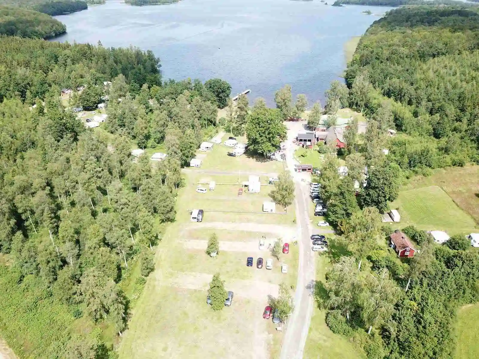 Flygfoto över Hätteboda Vildmarkscamping i ett naturskönt landskap med tät skog, strandområden och vatten drag.