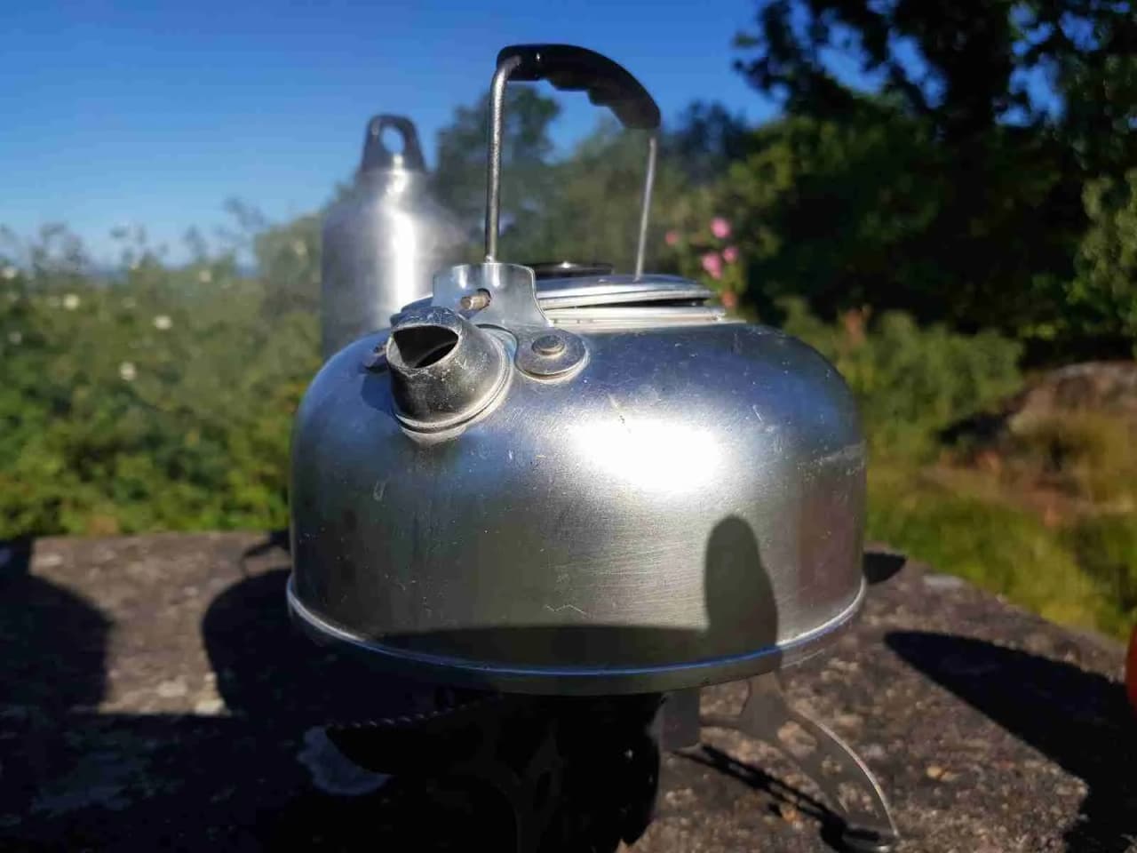 En campingplats med fokus på köksfaciliteter, där en silverfärgad vattenkokare och köksredskap syns i en husvagn eller campingmiljö.