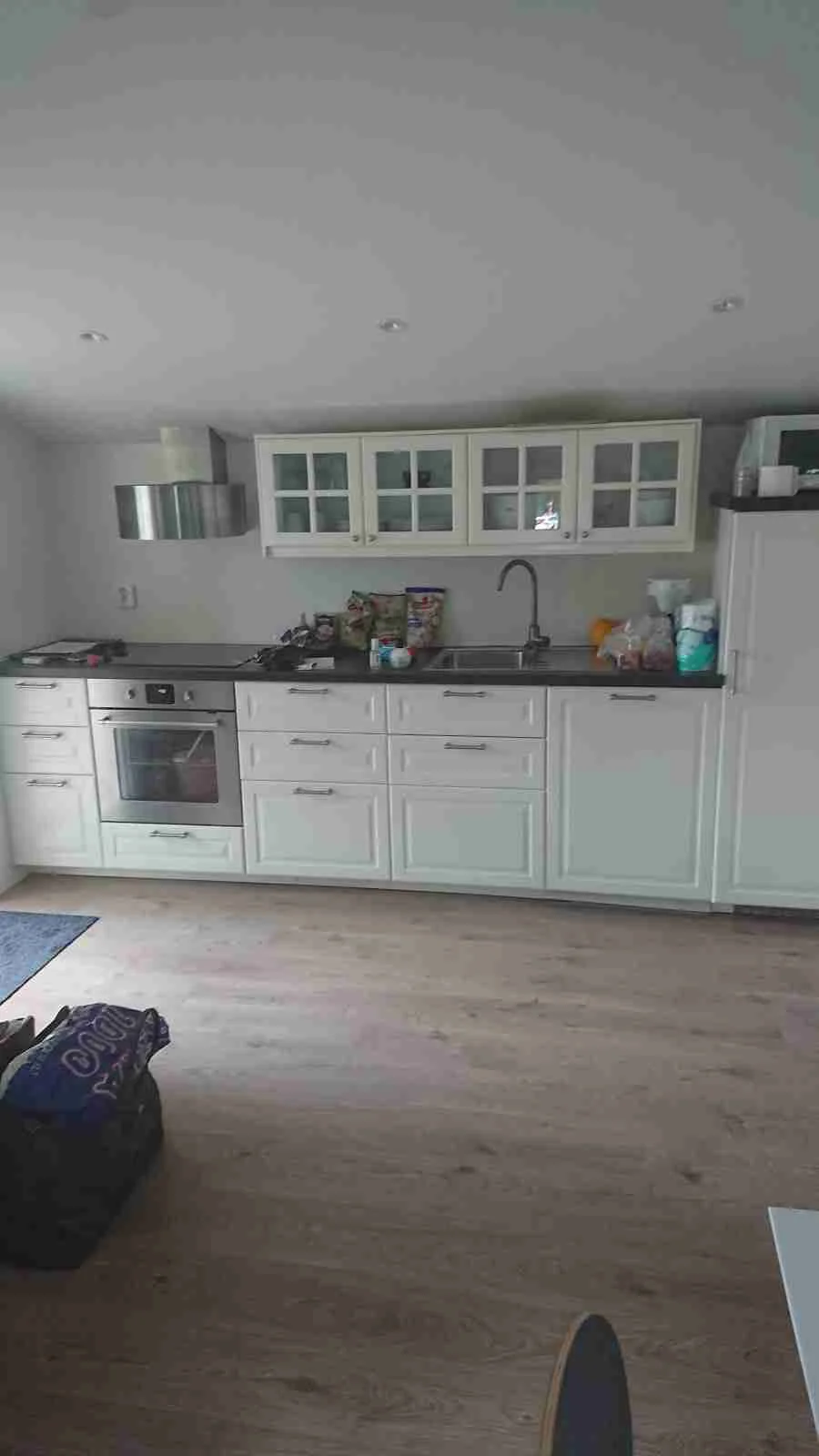 Ett modernt kök med trägolv, ljusa köksskåp och bänkskiva. Köket är utrustat med olika köksapparater och har en stilren inredning.