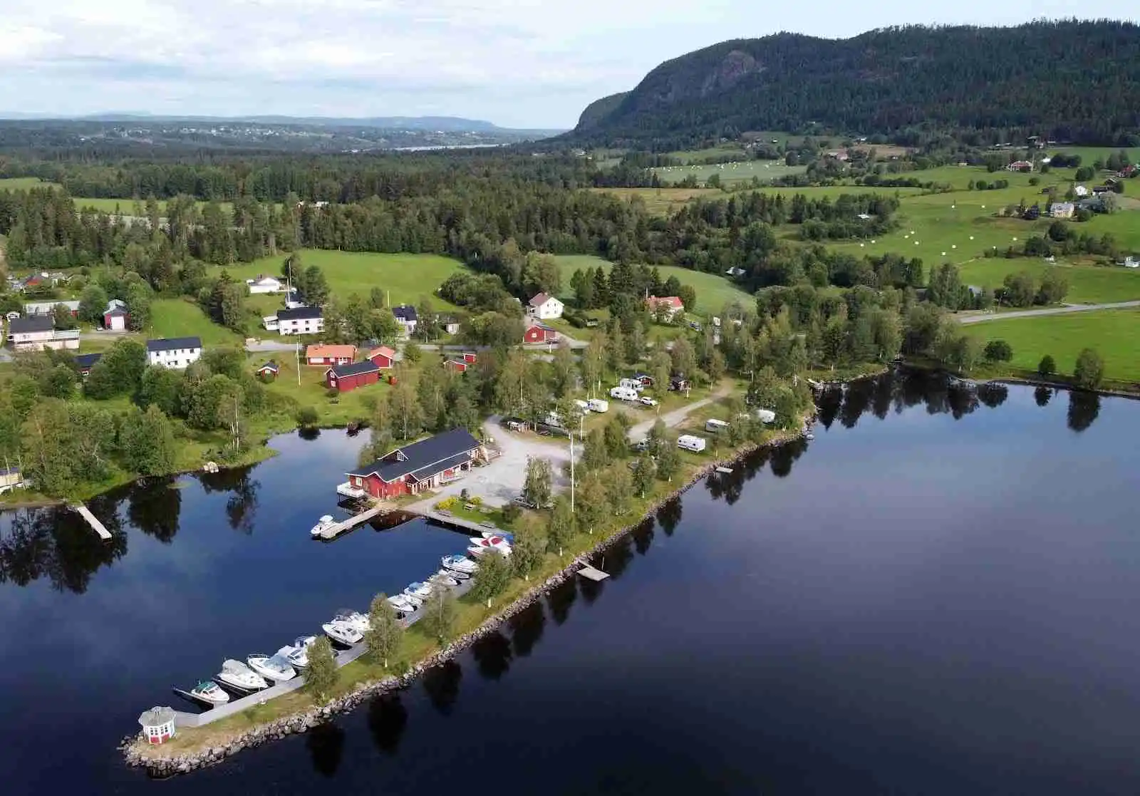 En naturskön campingplats vid en sjö med en liten stuga nära vattnet, omgiven av grönskande strand och träd.
