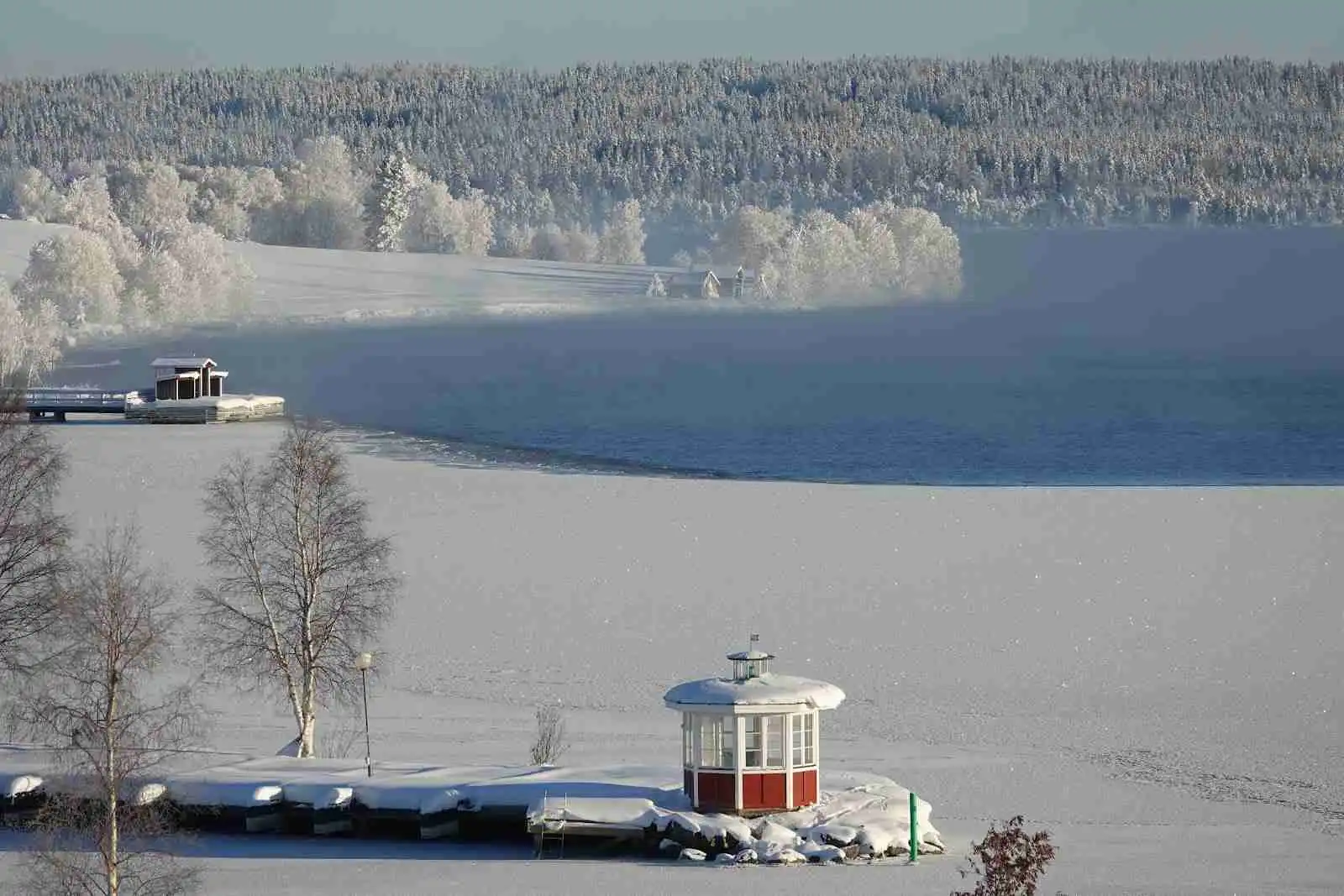 En frusen sjö täckt av snö, med en båt fastfrusen i isen vid Hoverbergs camping under vintertid.