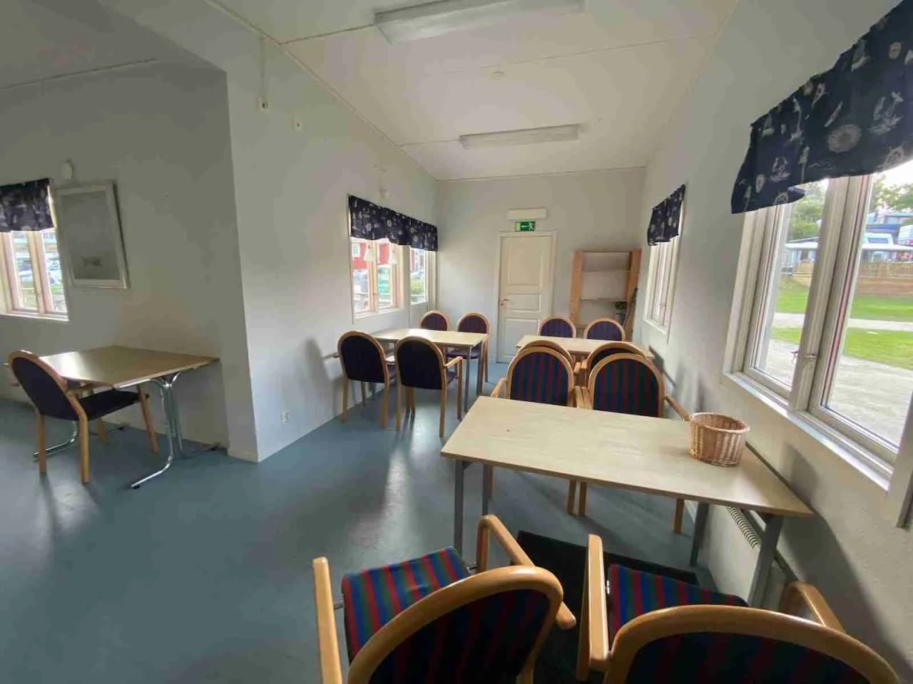 Ett interiörfoto från Marstrands familjecamping som visar ett ljust och luftigt rum med träinredning. Trägolv och trädetaljer matchar möblerna, däribland flera trästolar. Till vänster syns dagsljus som strömmar in genom fönstren, vilket bidrar till den hemtrevliga stämningen.