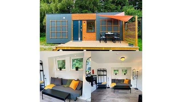 En solig dag på Lomma Camping med en mobil hem placerad vid sidan av ett skuggigt grönområde. En uteplats med trädgårdsbord och stolar står i förgrunden, omgiven av frodig natur.