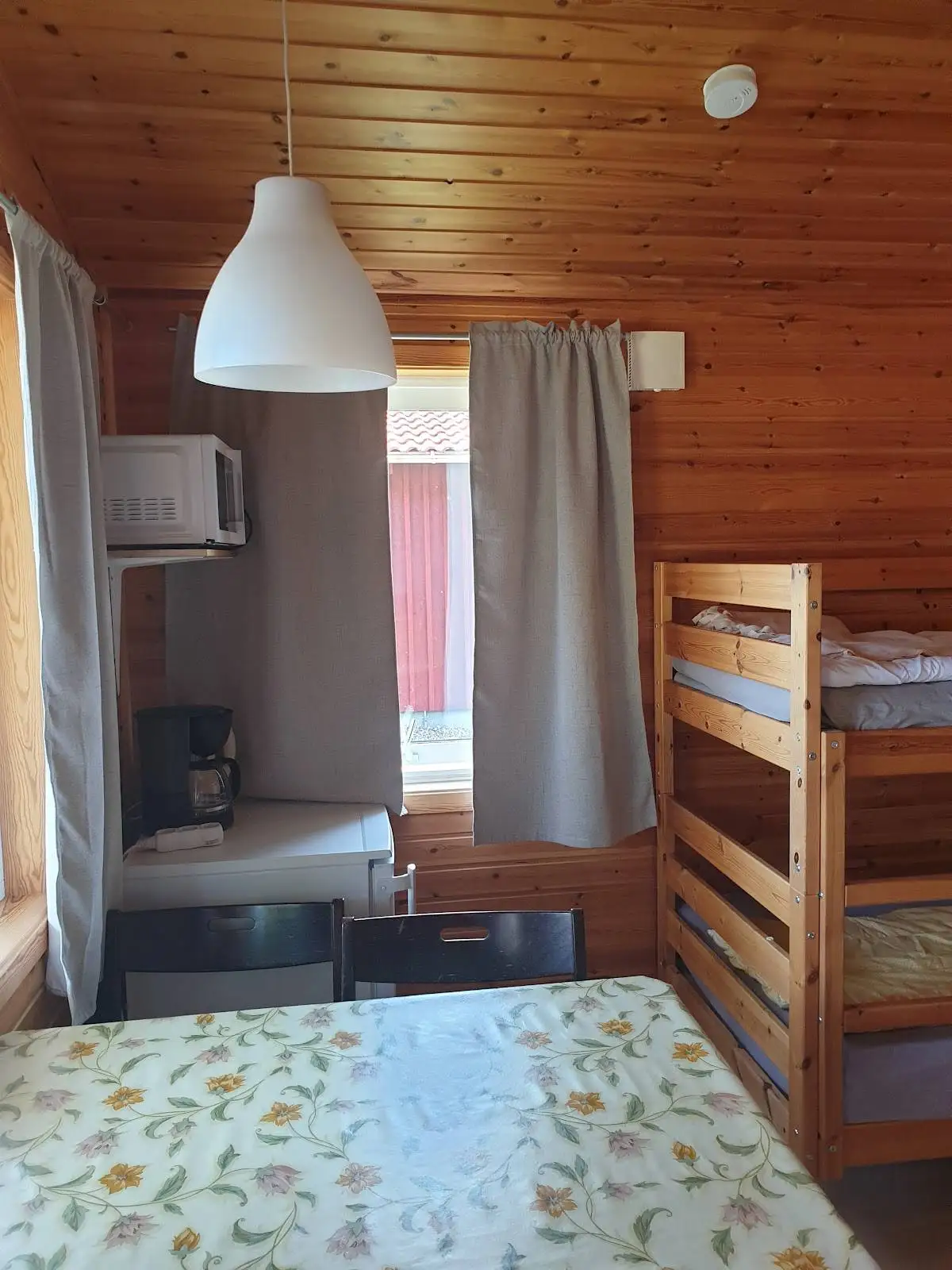 Alt-text: Ett interiörfoto från Kosta Bad och Camping som visar ett rum med trägolv och trädetaljer. Taklampan sprider ljus över det enkelt inredda utrymmet, där trä går igen i möbler, golv och tak.