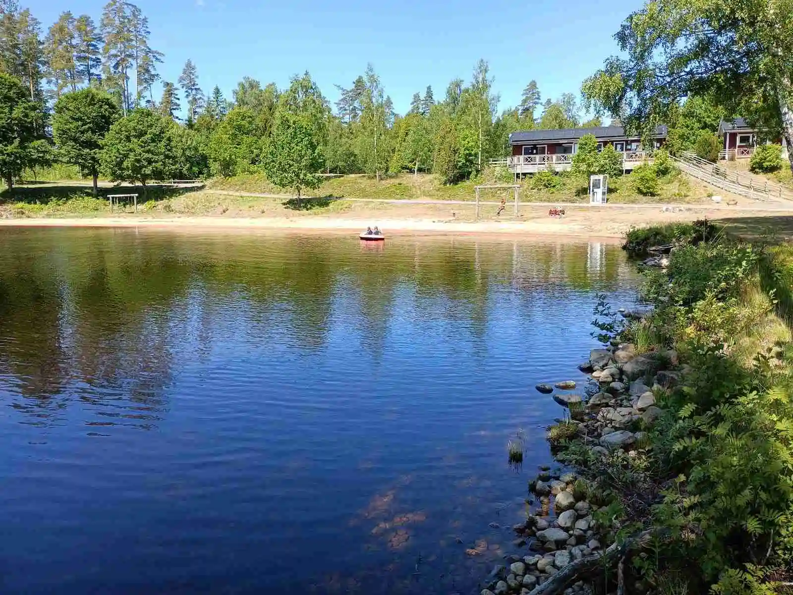 Bild av Löckna Camping: En somrig och fridfull miljö med en vattenspegel omgiven av grönska. Träd och växtlighet kantar den lilla vattenvägen, vilket skapar en inbjudande atmosfär. Perfekt för besökare som söker naturupplevelser.
