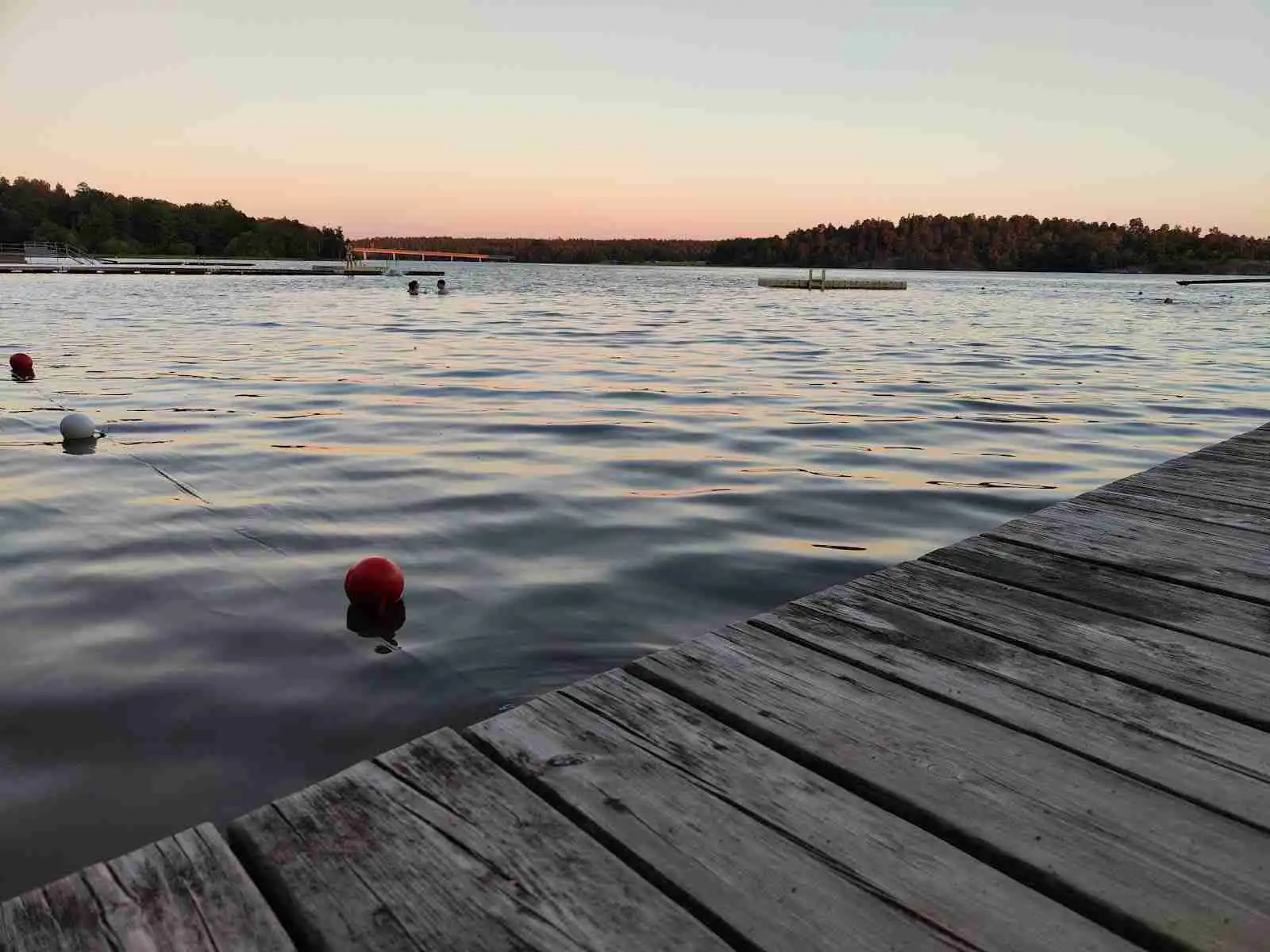 Bild av en lugn vattenyta med en vidsträckt horisont. Bakgrundens mjuka skymningsfärger speglar sig i sjön. Perfekt för rekreation och avkoppling vid Ängby camping.