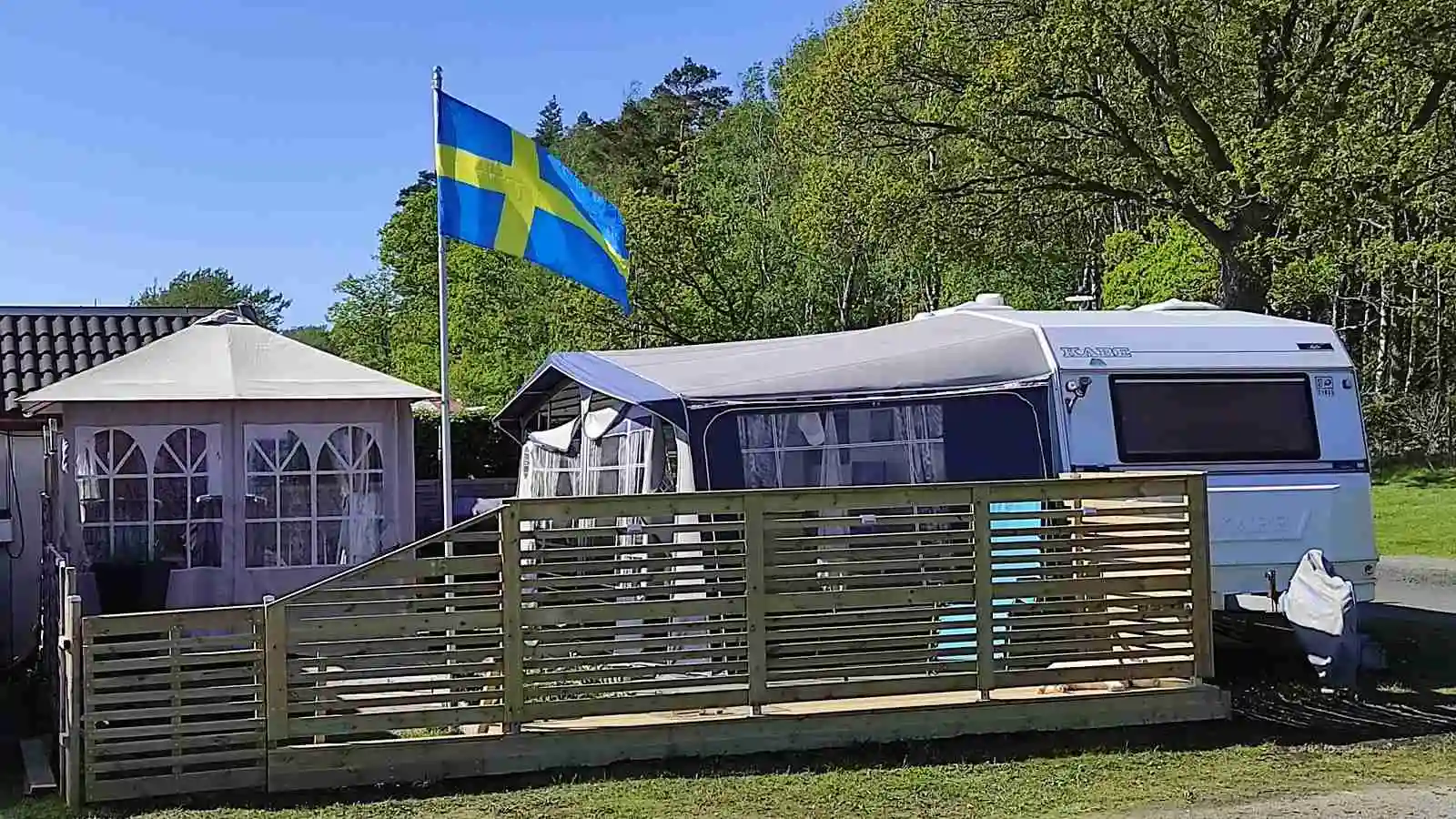 Bild av Stråvalla Camping som visar en grönskande gård med husvagnar, husbilar och tält uppställda. En lastbil står parkerad i närheten, vilket skapar en inbjudande atmosfär för camping och friluftsliv.