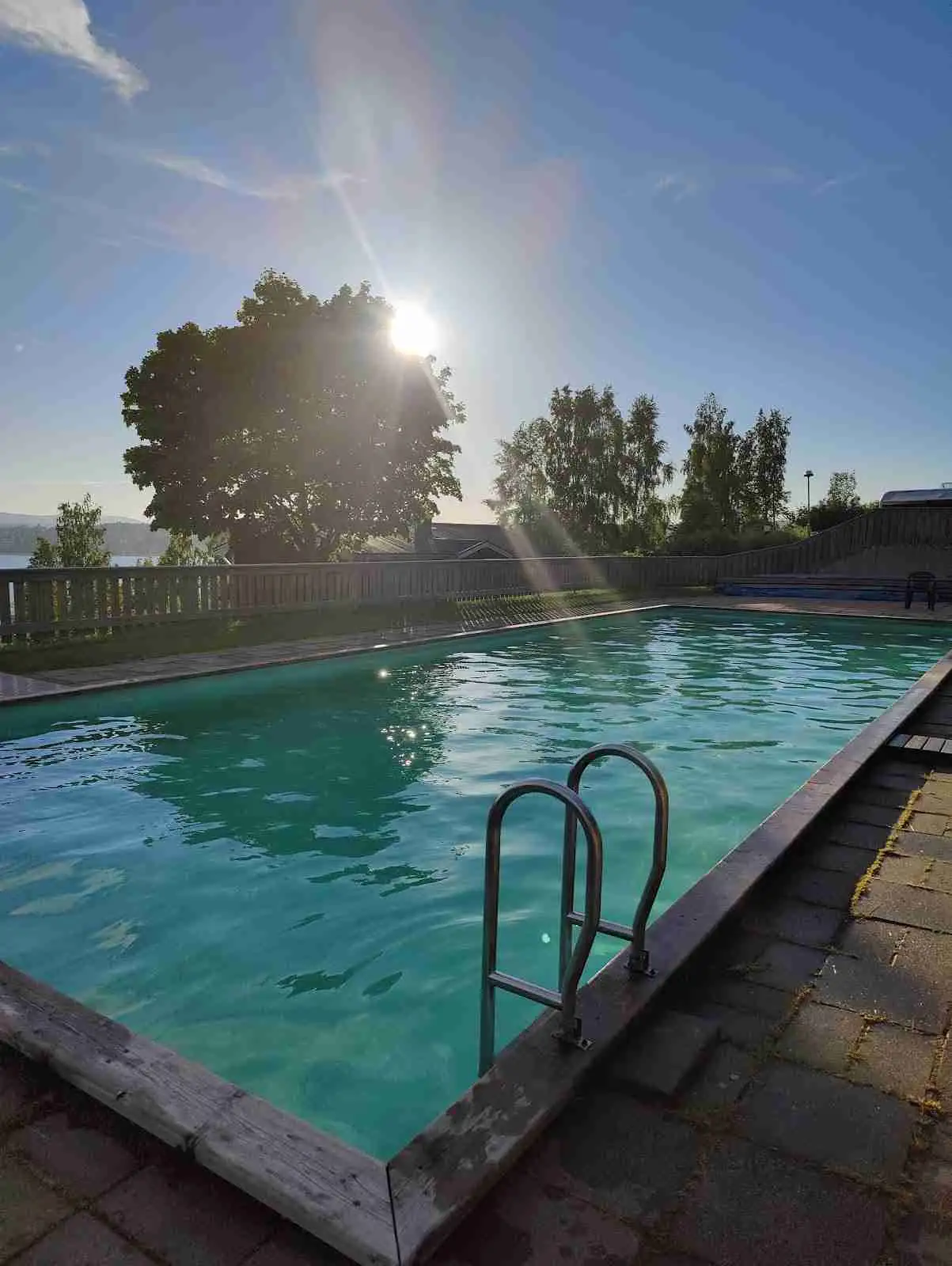 En pool vid ett semesterresort i Solbacken, omgiven av vatten och fritidsområden. Kvällssolens sken reflekteras på den lugna vattenytan, vilket skapar en avkopplande och inbjudande atmosfär för besökare.