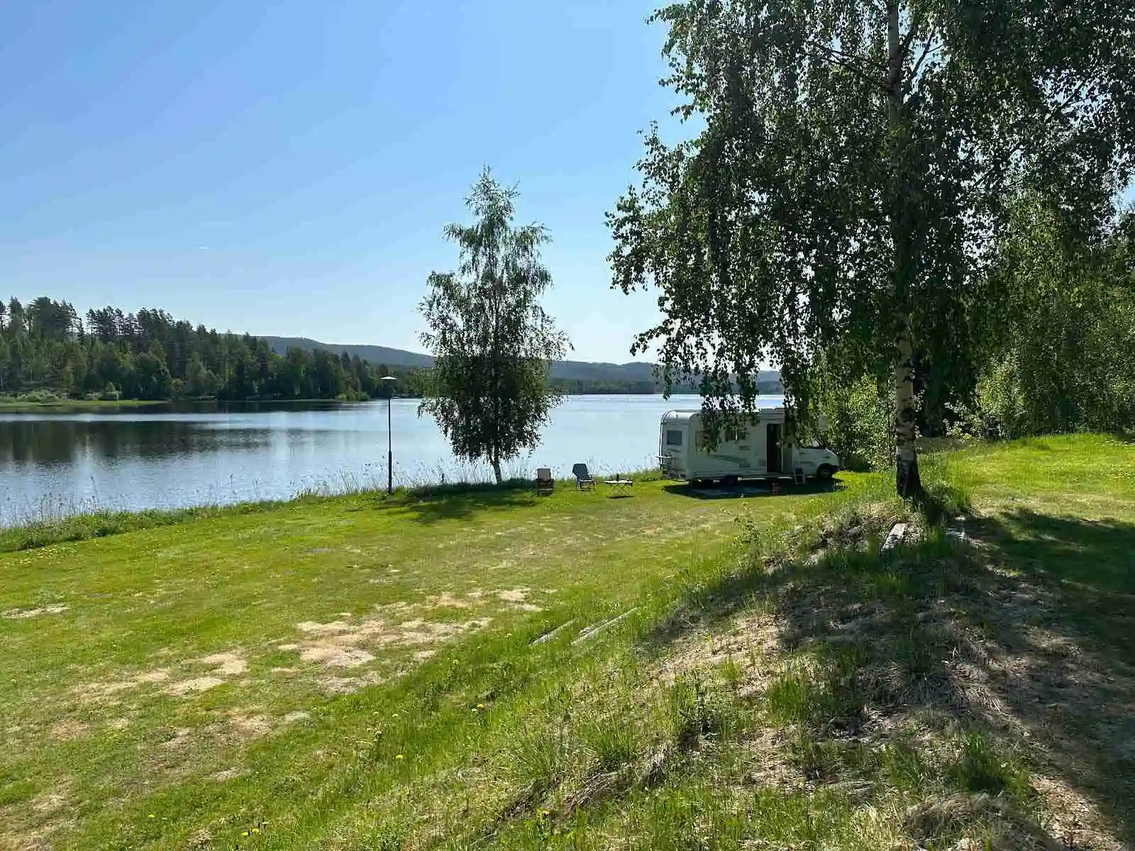 Bild av en naturskön campingplats i Fristad, belägen vid en lugn sjö omringad av grönskande flodlandskap och en park.