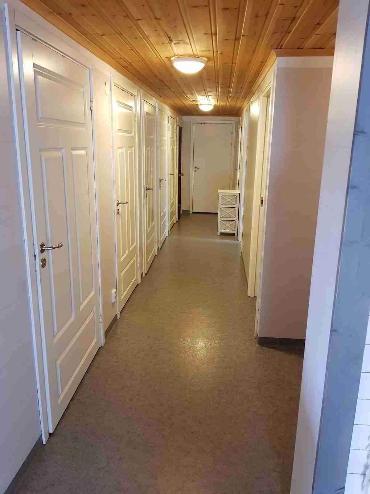 Interiör av en stuga på Järvsö Bergscamping med trägolv, träväggar och trätak. En dörr syns i rummet tillsammans med kakelbeläggning och trädetaljer.