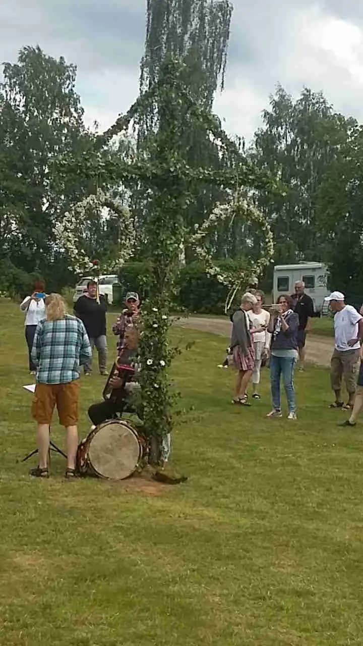 Bild av Linneryds camping som visar en grönskande gräsmatta omgiven av träd. Besökare kan ses njuta av fritidsaktiviteter i parkområdet, vilket skapar en avkopplande semesteratmosfär. En flaggstång är synlig i bakgrunden och bidrar till den natursköna utsikten.