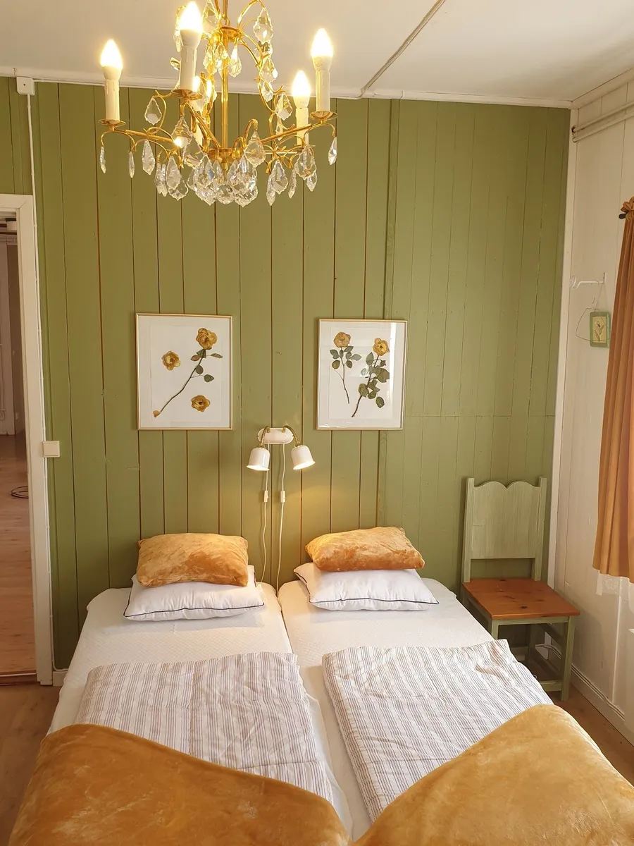 Ett mysigt sovrum inrett med ljusa träväggar och trägolv. Det finns en stilren säng med vita textilier i centrum av rummet. Taket består av träpanel och det finns sparsam dekoration, vilket ger rummet en varm och inbjudande atmosfär.