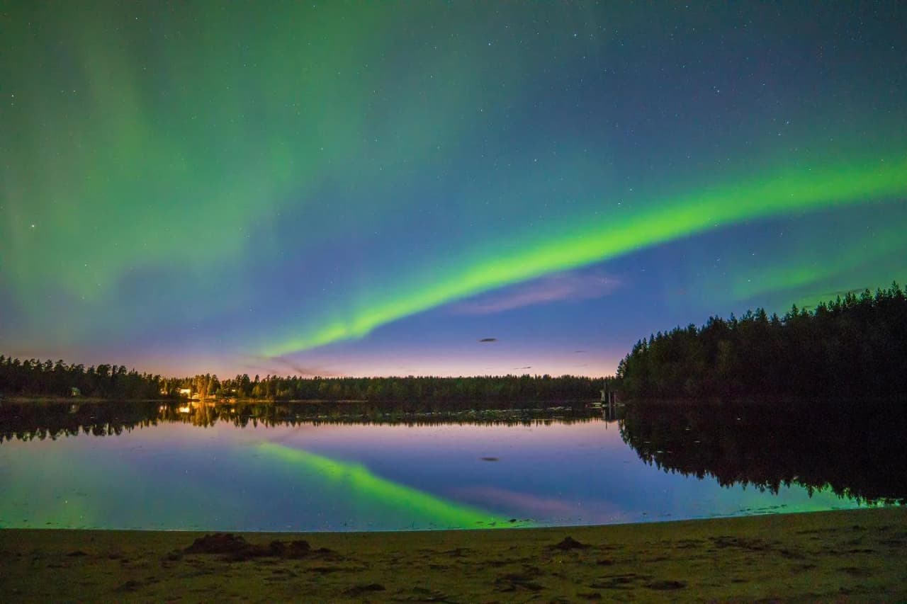 En vacker kvällsutsikt över Seskarö havsbad & camping med en spegelblank sjö omgiven av grönska. Himlen reflekteras i vattnet och skapar en lugn och fridfull atmosfär.