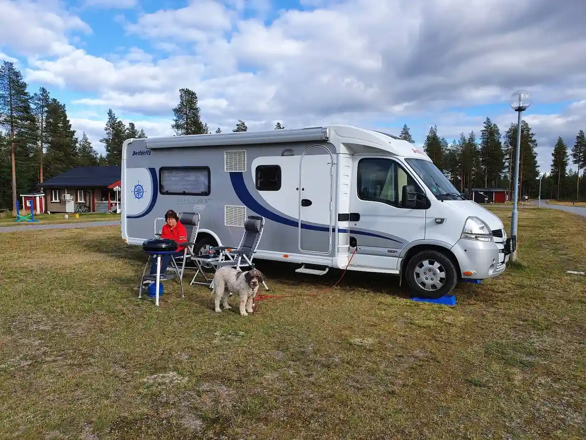 En parkerad husvagn med flera kringliggande campingfordon på Fromhedens camping, omgiven av grönska och en öppen yta.